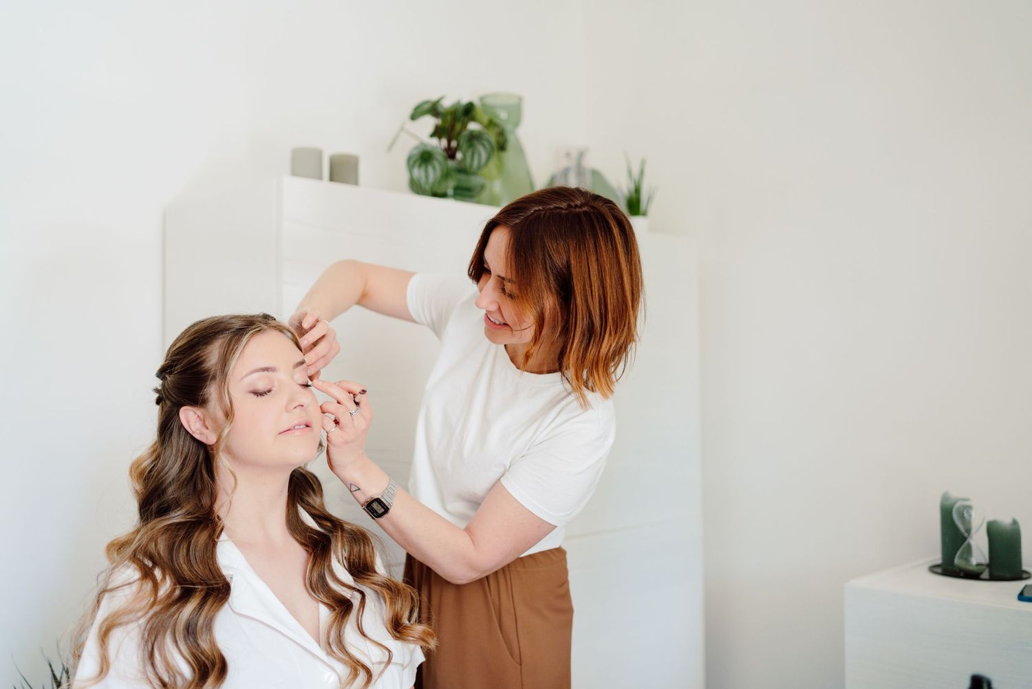 Hair stylist carefully arranging the bridal hairstyle of a smiling bride in a bright salon.