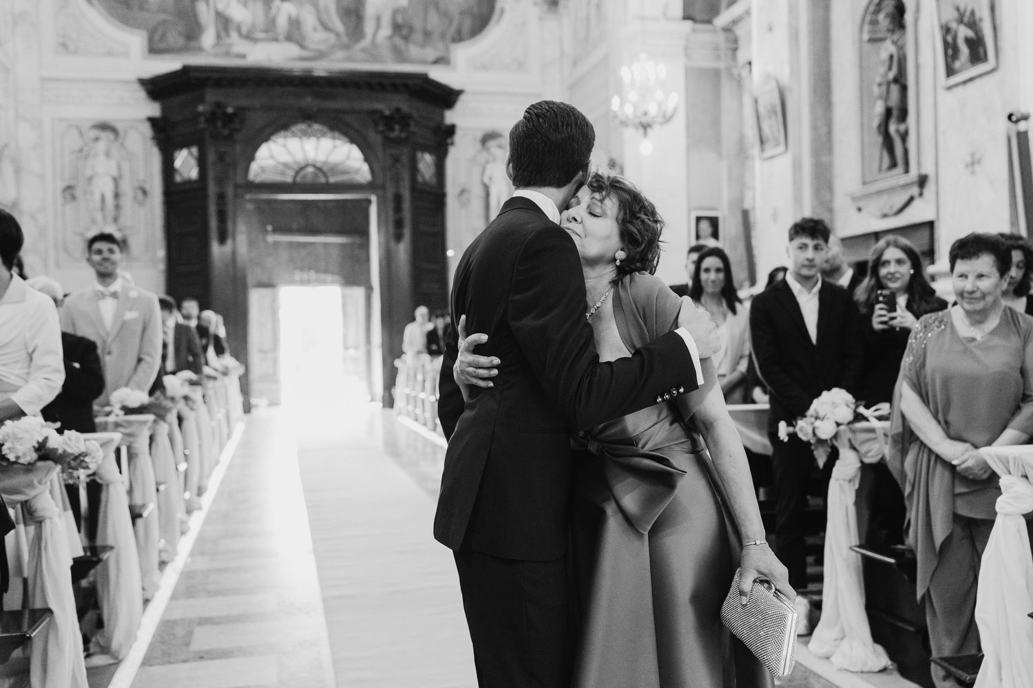 Black and white photo of a couple sharing a first kiss at the altar in a church.