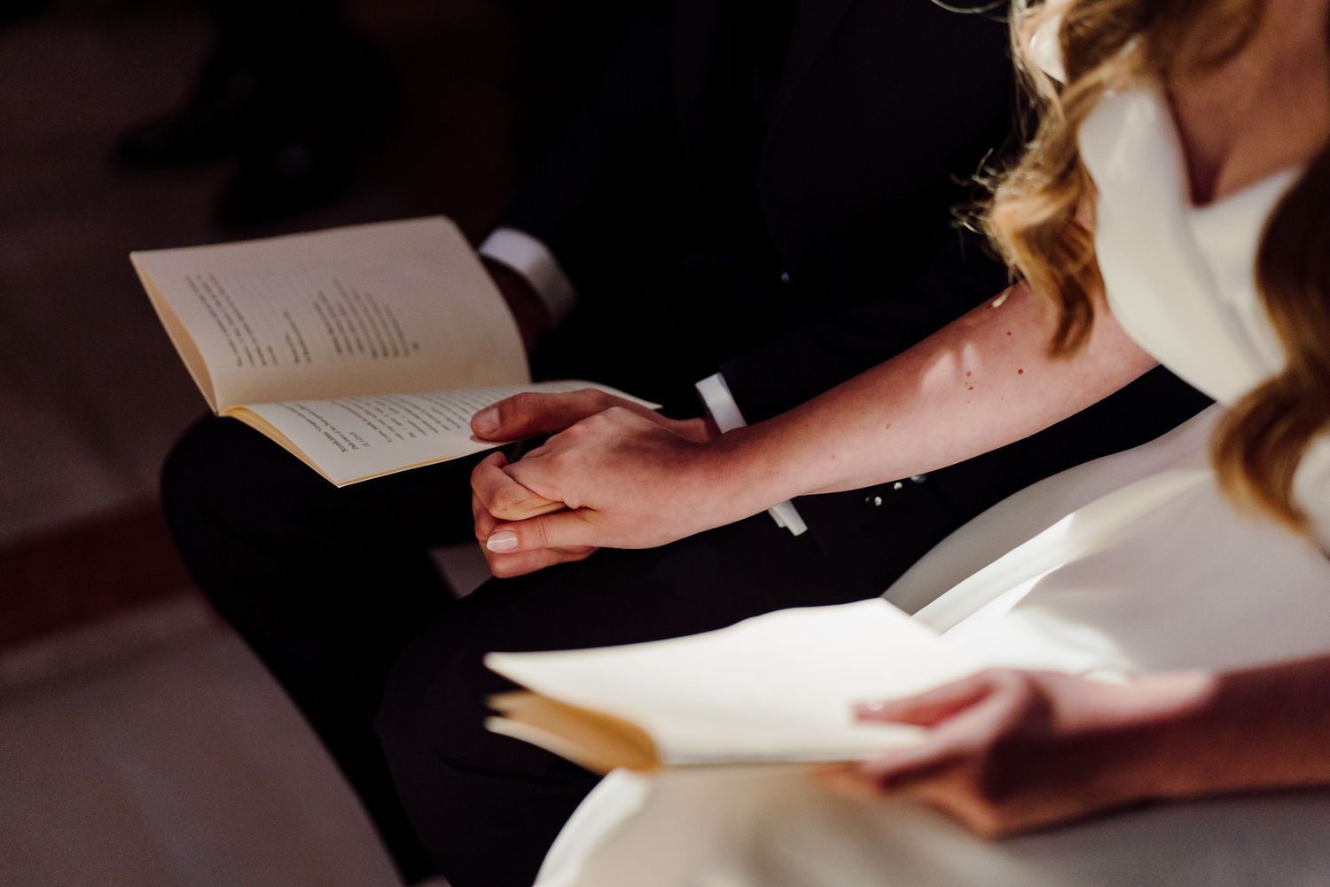 Wedding guests hold ceremony programs while sitting in church pews during the service.