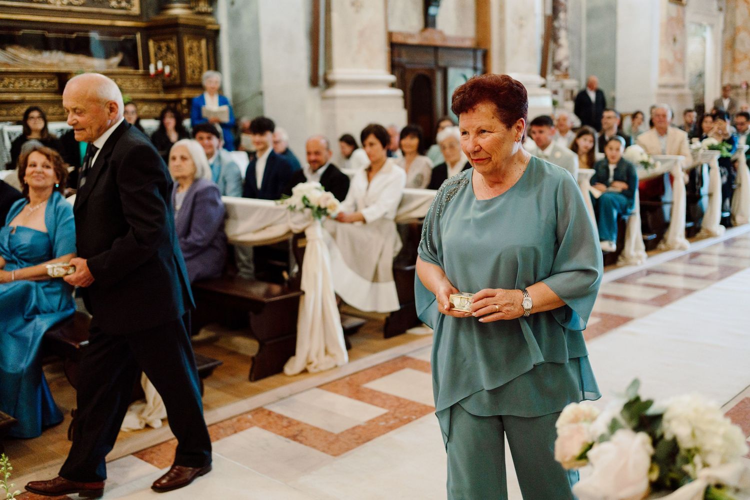 Wedding guests process through decorated church aisle during a formal Catholic ceremony.