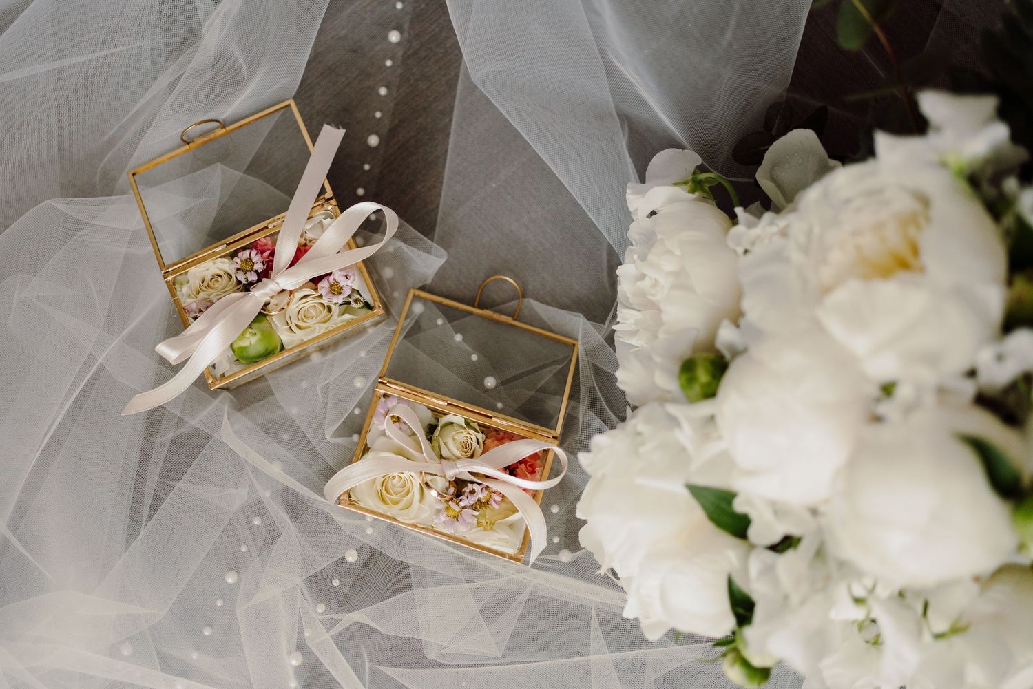 Two gold geometric ring boxes with wedding rings beside a white peony bridal bouquet.