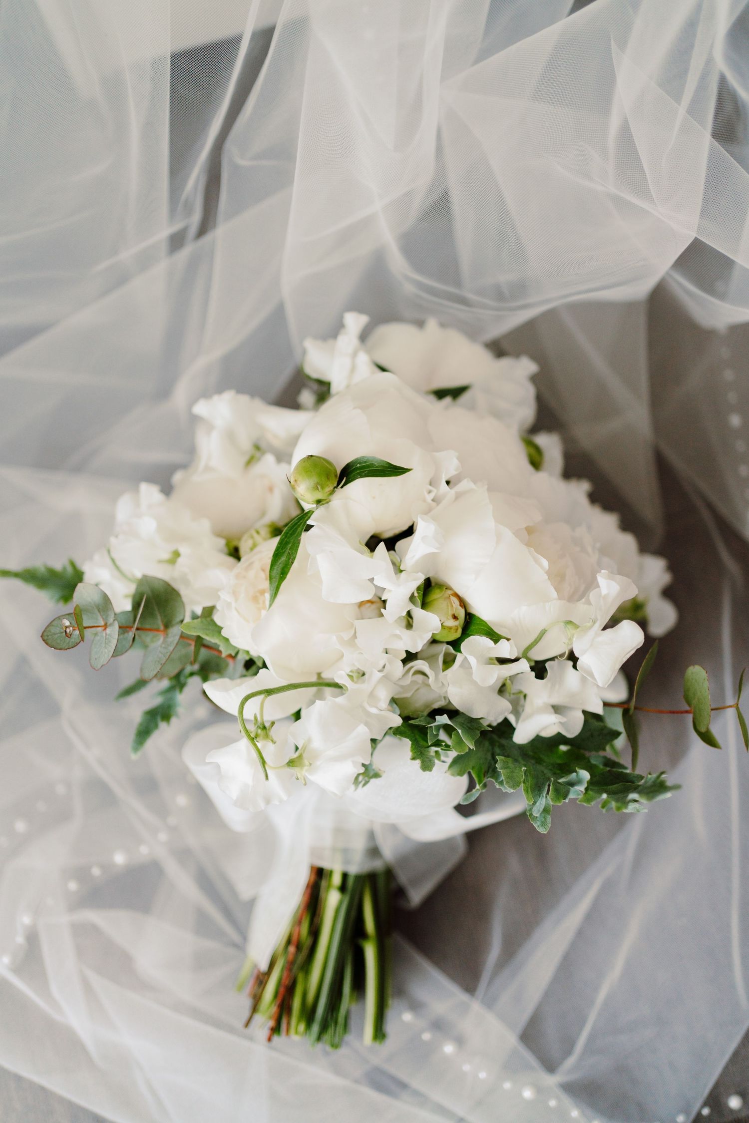 Elegant white wedding bouquet of roses and sweet peas resting on a delicate sheer veil.