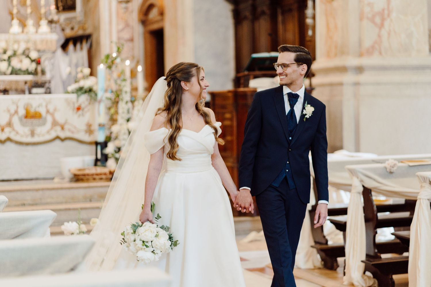 Newlyweds walk hand in hand through beautifully decorated church after their ceremony.
