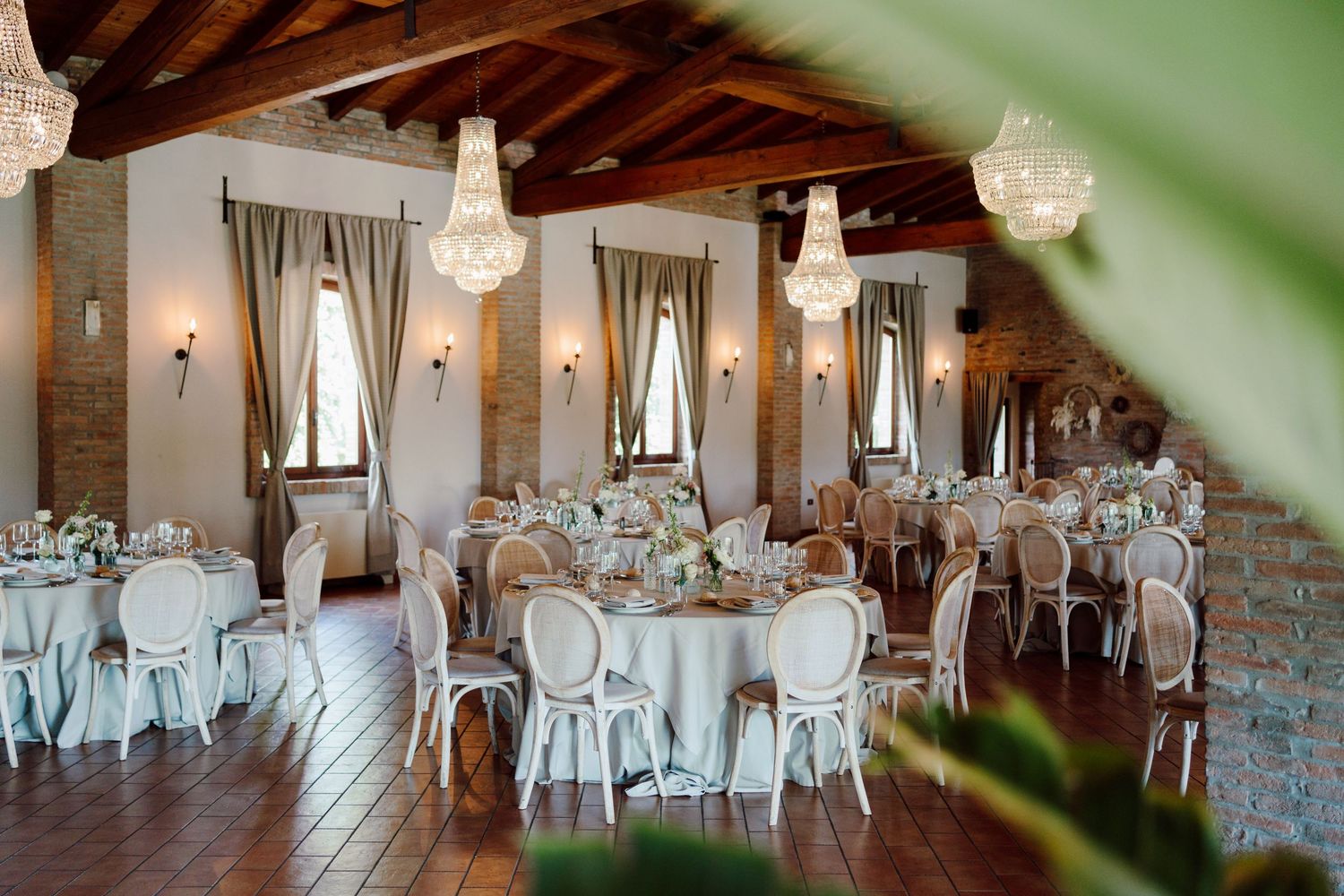 Elegant rustic wedding reception hall with crystal chandeliers and white round tables.