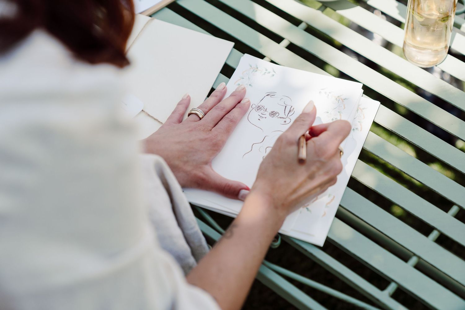 Artist sketching a portrait in a notebook at an outdoor wedding caricature station.
