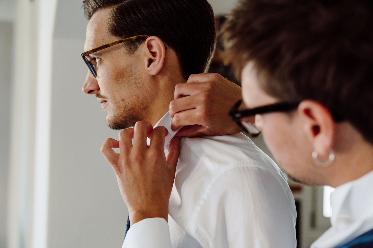 Close-up of a groomsman helping a smiling groom adjust his collar before the wedding.