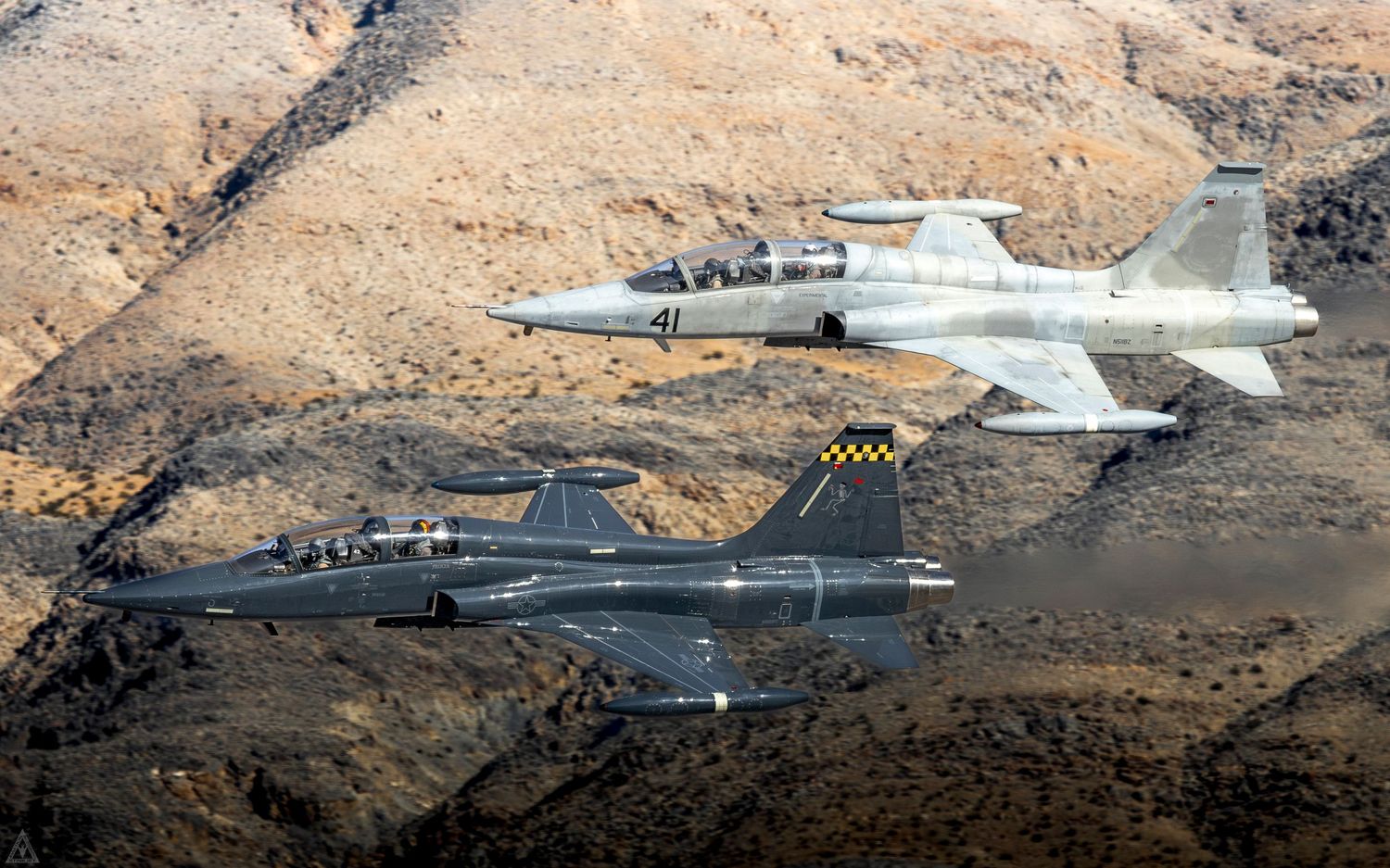 Two CF-5Ds fly in close formation with desert mountains rising in the background