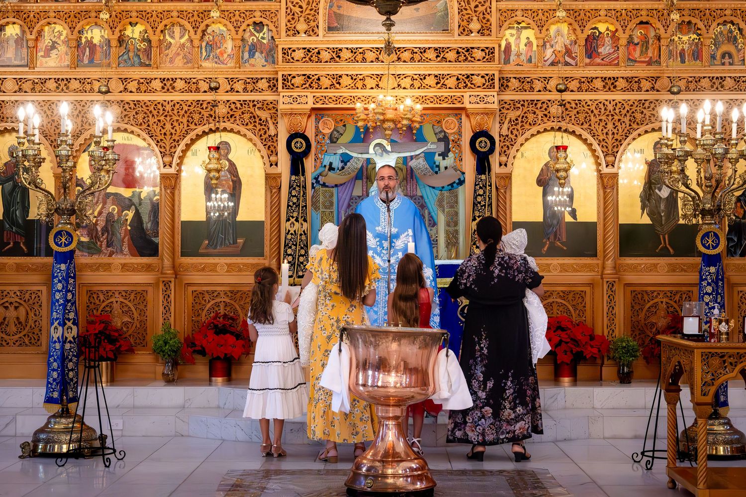 Orthodox priest performs a baptism ceremony at an ornate golden iconostasis altar with children and family present.