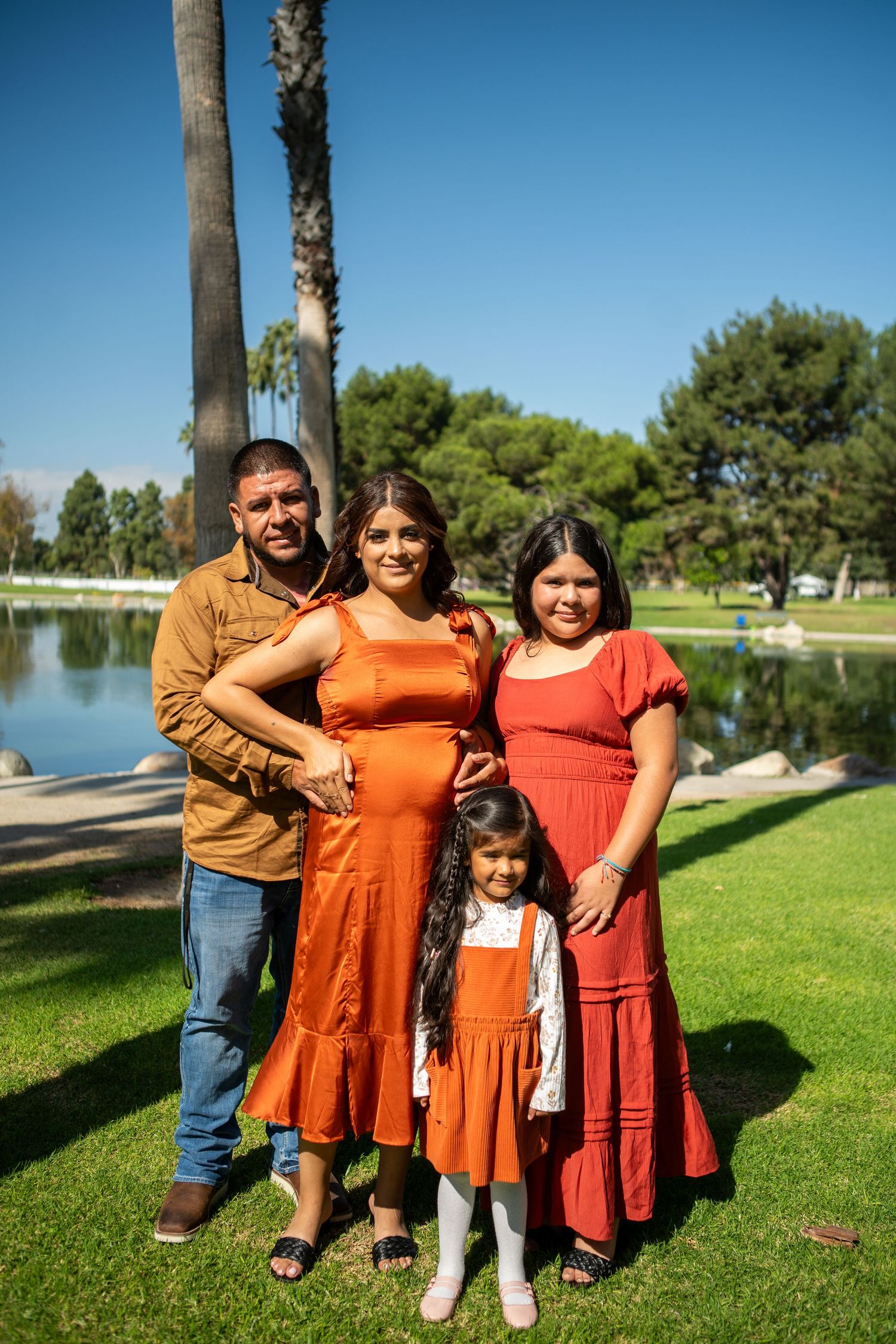 A family poses together on a sunny day by a lake with palm trees and green grass in the background.