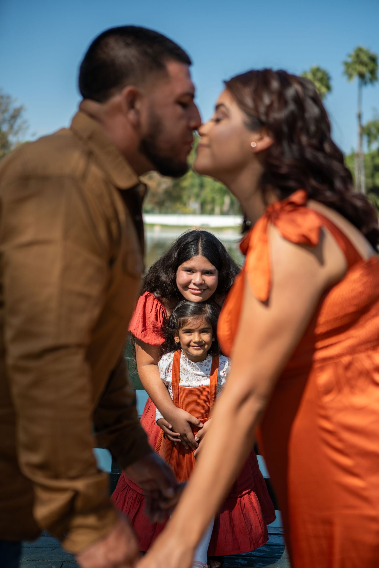 A couple shares an intimate moment while a young girl in a red dress smiles in the background.