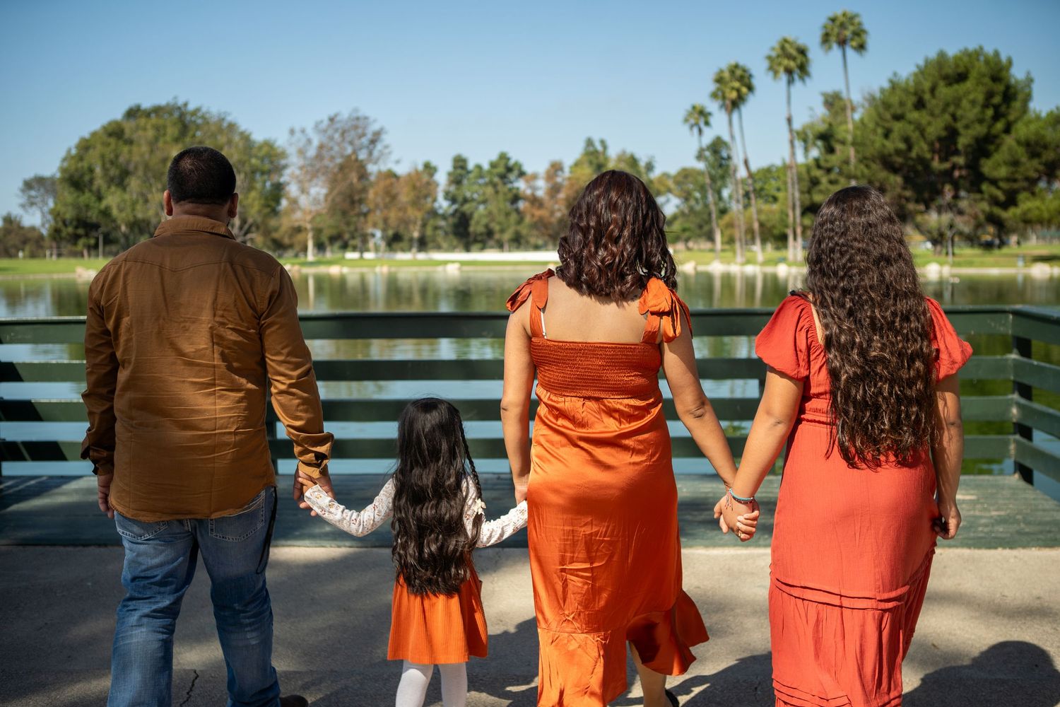A group of people in coordinating orange and brown outfits pose together by a lake in a park setting.