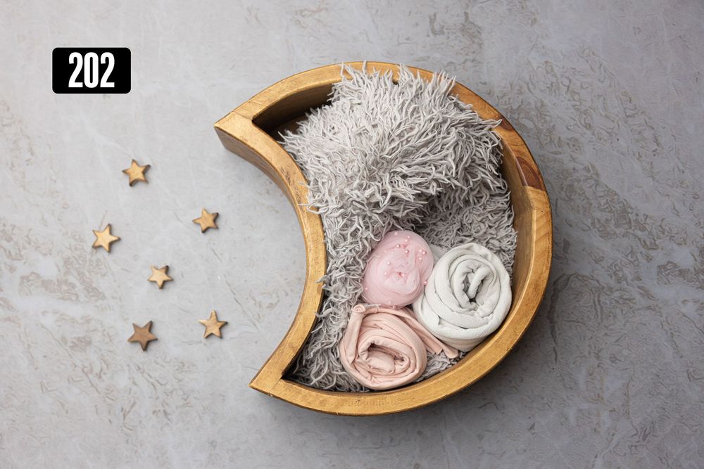 Wooden moon-shaped bowl with gray fur, pink and white wraps, and star props for newborn photos.