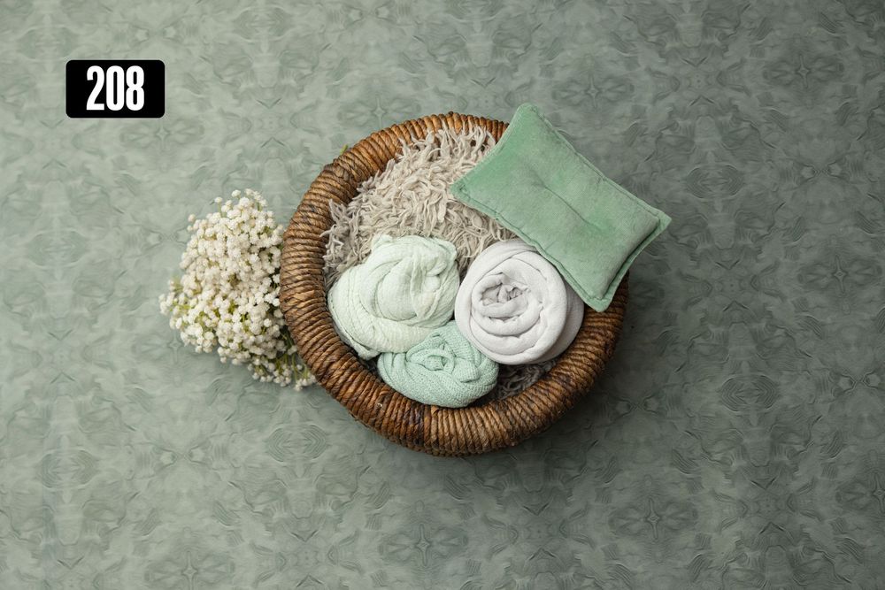 Wicker basket with sage green rolled wraps, small pillow, and baby's breath on a green damask backdrop.