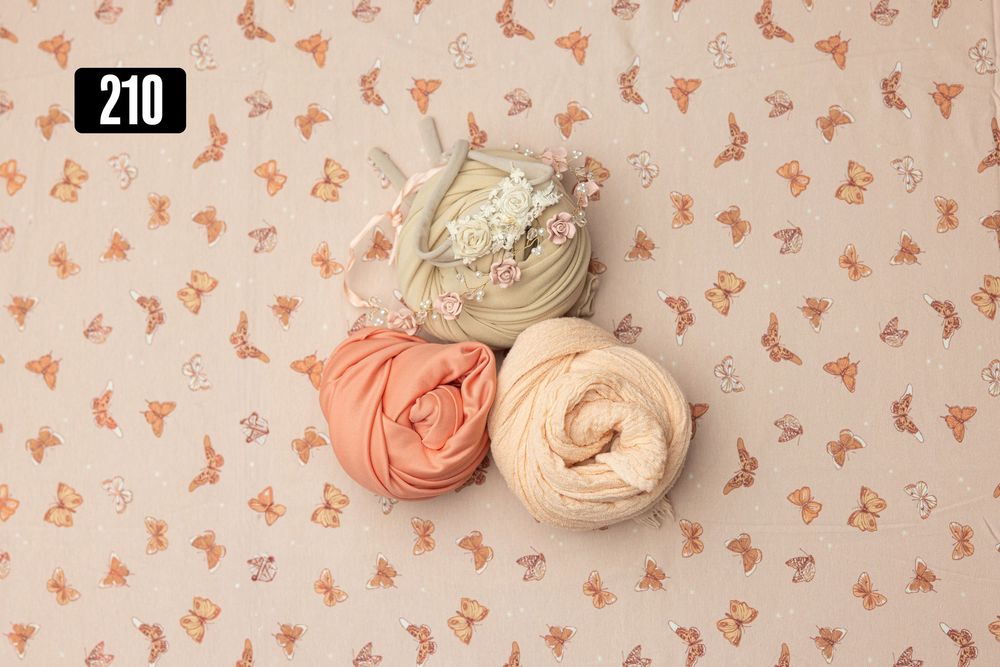 Three rolled fabric wraps in sage, coral, and cream on a cream butterfly-print newborn photography backdrop, number 210.