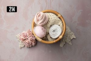 Wooden bowl with pink roses, lace, and soft wraps on a dusty rose background for newborn photography.