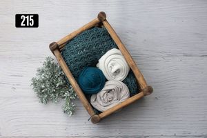 Wooden crate with teal knit wrap, white rolled wraps, and dusty blue greenery for newborn photography.
