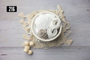 Neutral toned newborn photography props including a white knit bowl, yarn rolls, and wooden beads on macrame mat.