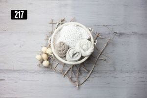 White knit newborn hat and rosette wraps in a bowl with wooden beads on rustic wood background.