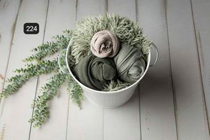 Sage green fabric wraps and floral elements arranged on white wooden planks.