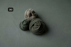 Minimalist arrangement of dark gray fabric wraps on muted green background.
