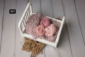 White miniature bed with pink fabric wraps and textured blanket on wooden floor.