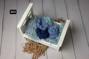Small white bed filled with blue fabric wraps and fluffy gray blanket on wooden floor.