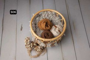Neutral-toned fabrics and textures displayed in wooden bowls on a white wooden surface.