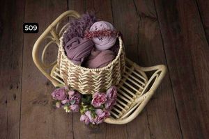 Woven basket with purple fabrics and pink flowers arranged on dark wooden floor.