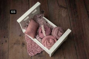 White wooden crate filled with dusty rose colored textiles on wooden surface.