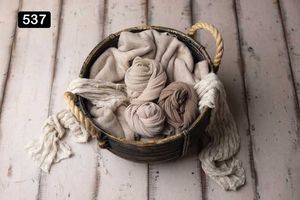Neutral colored fabric roses and textiles displayed in woven baskets on white wooden planks.
