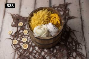 Yellow and cream colored textiles arranged in vintage baskets on distressed wood surface.