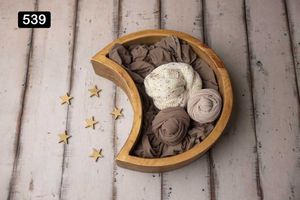 Crescent-shaped wooden bowl filled with neutral colored fabric wraps and decorative gold stars on wooden backdrop.