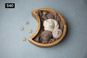 Moon-shaped wooden bowl containing brown and white fabric wraps with small gold stars on gray surface.
