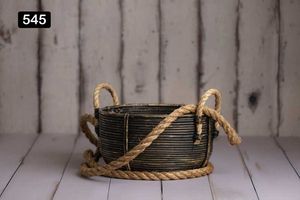 Dark woven basket with rope handles on white wooden floor.