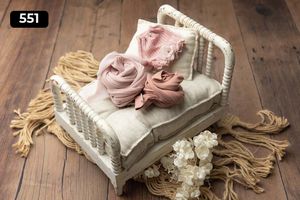Vintage white wicker bed prop with pink fabric wraps and floral accents on wooden floor.