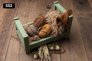 Rustic green wooden bed prop filled with brown fabric wraps and dried wheat decorations.