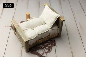 Small wooden bed prop with white tufted cushioning on light wooden surface.