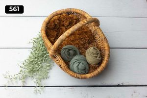 Woven basket with sage green fabric wraps and dried floral accents on white wooden surface.