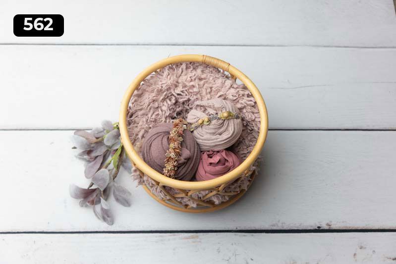 Round woven basket containing mauve fabric wraps with dried flower decoration.