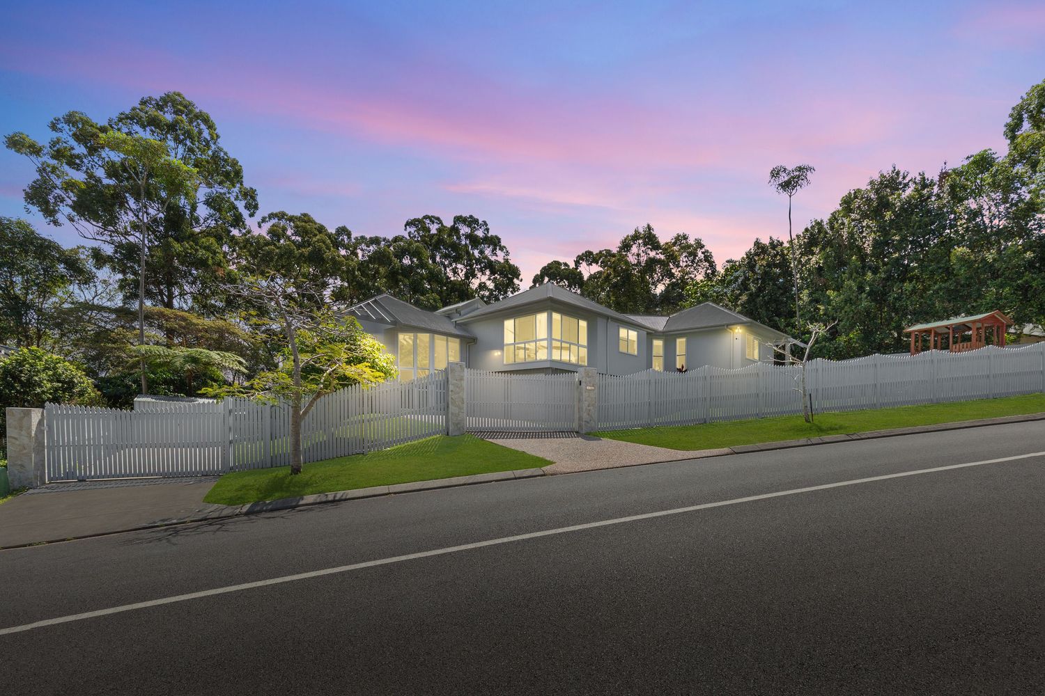 Spacious white rendered home with double garage, lush gardens, and tall eucalyptus trees at dusk.