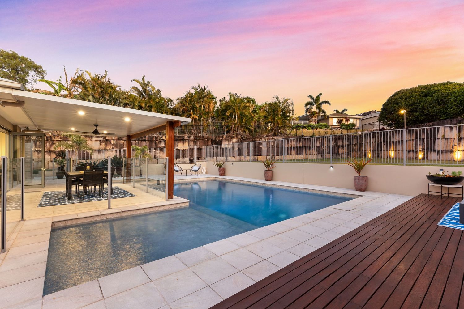 Elegant outdoor pool with timber decking, covered alfresco dining area, and colorful evening sky.