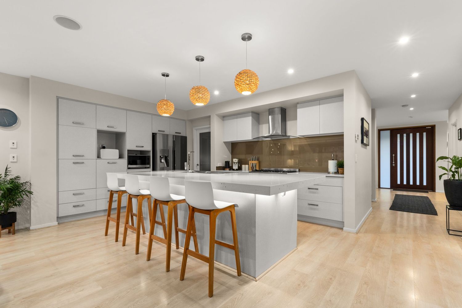 Modern open-plan kitchen with white cabinetry, island bench, bar stools, pendant lights, and timber floors.