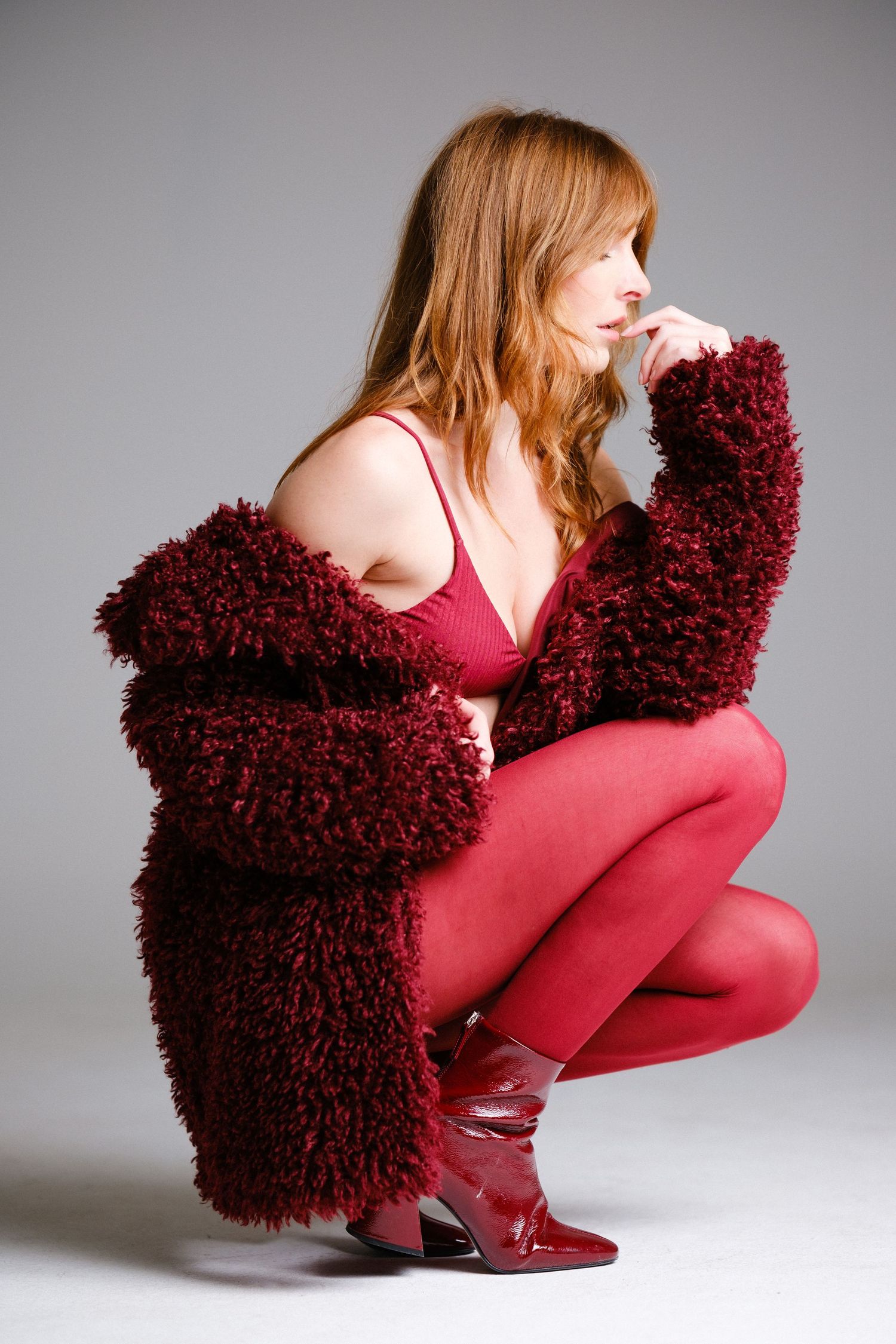 Artistic fashion pose with burgundy plush cushion and red bodysuit.