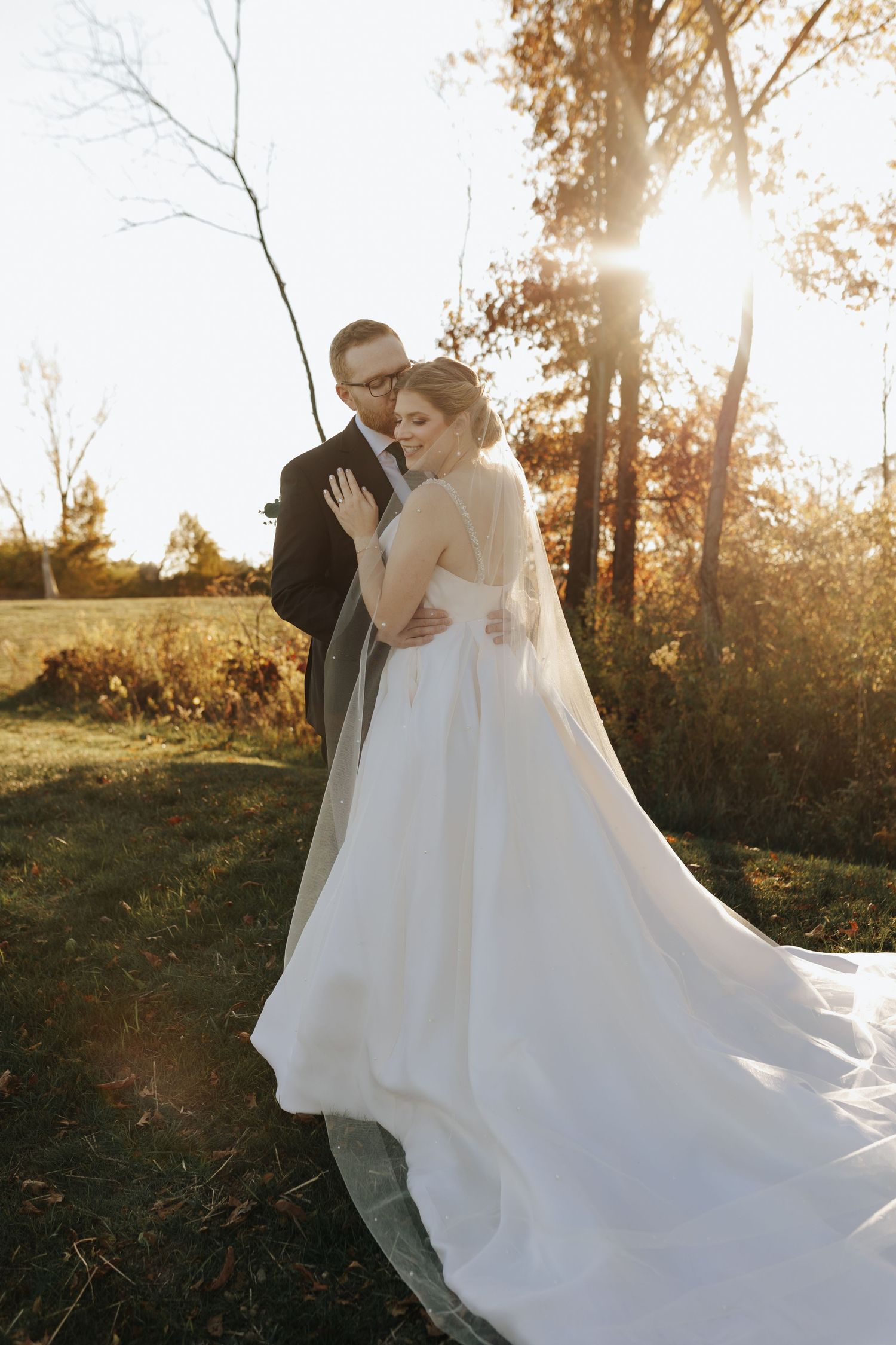 A romantic sunset wedding photo featuring a couple embracing outdoors with golden light filtering through autumn trees.