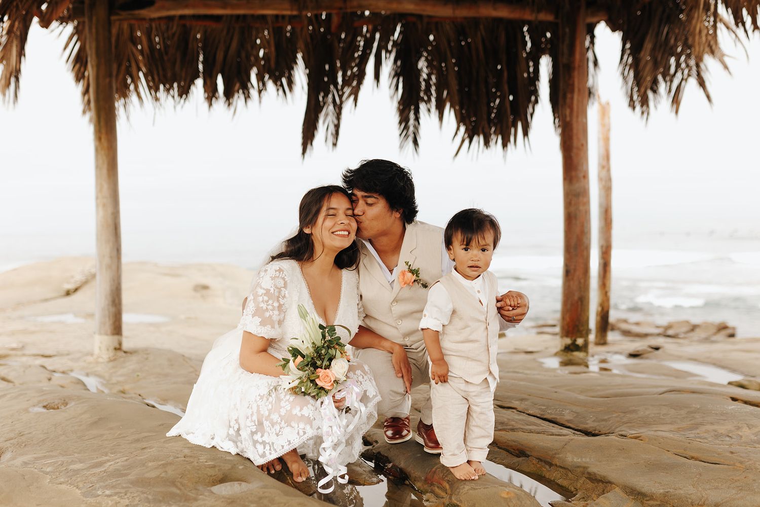 A family wearing all white sits under a thatched palapa on a peaceful beach at sunrise.