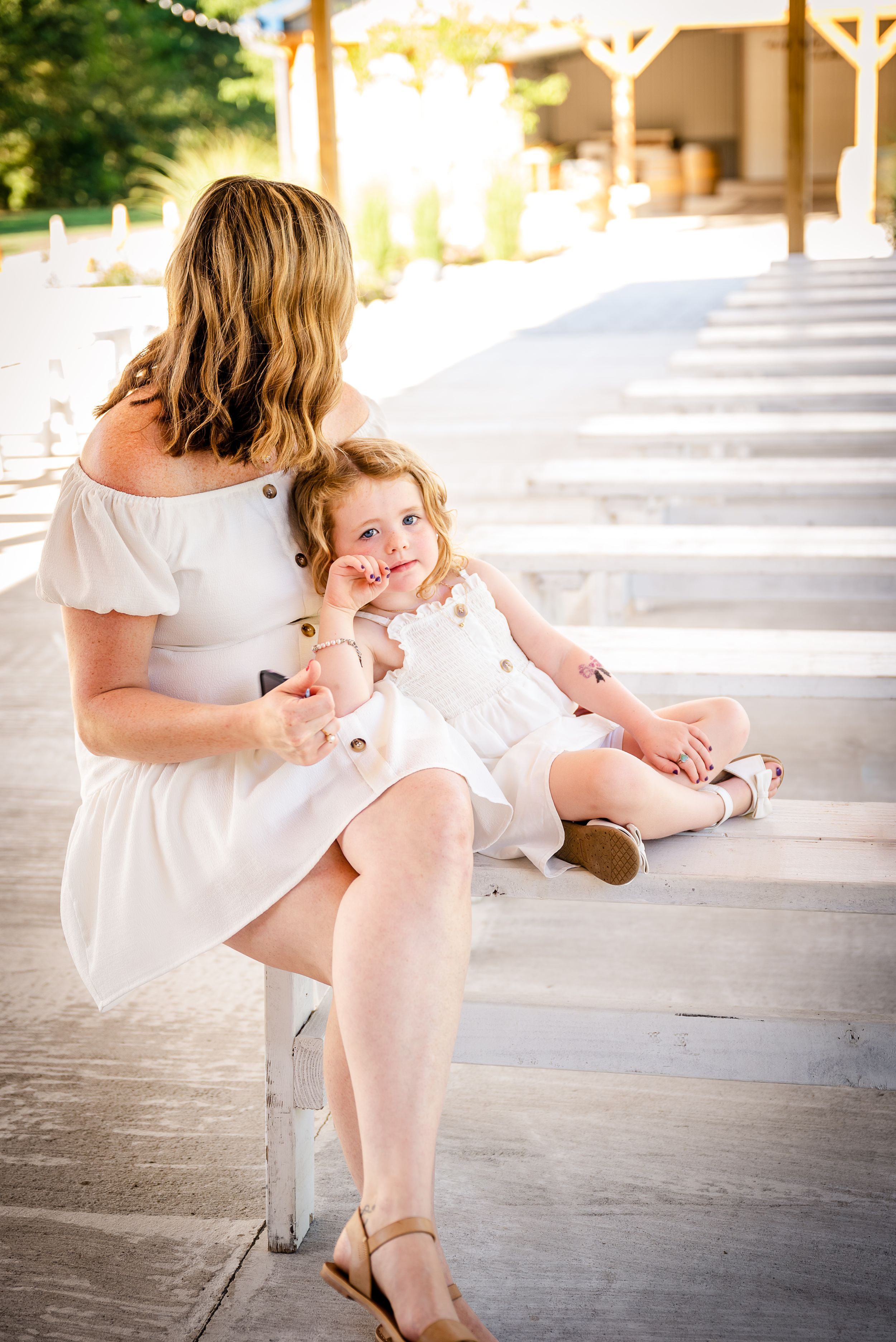 Mother and daughter in matching white dresses sitting together on outdoor steps in summer.