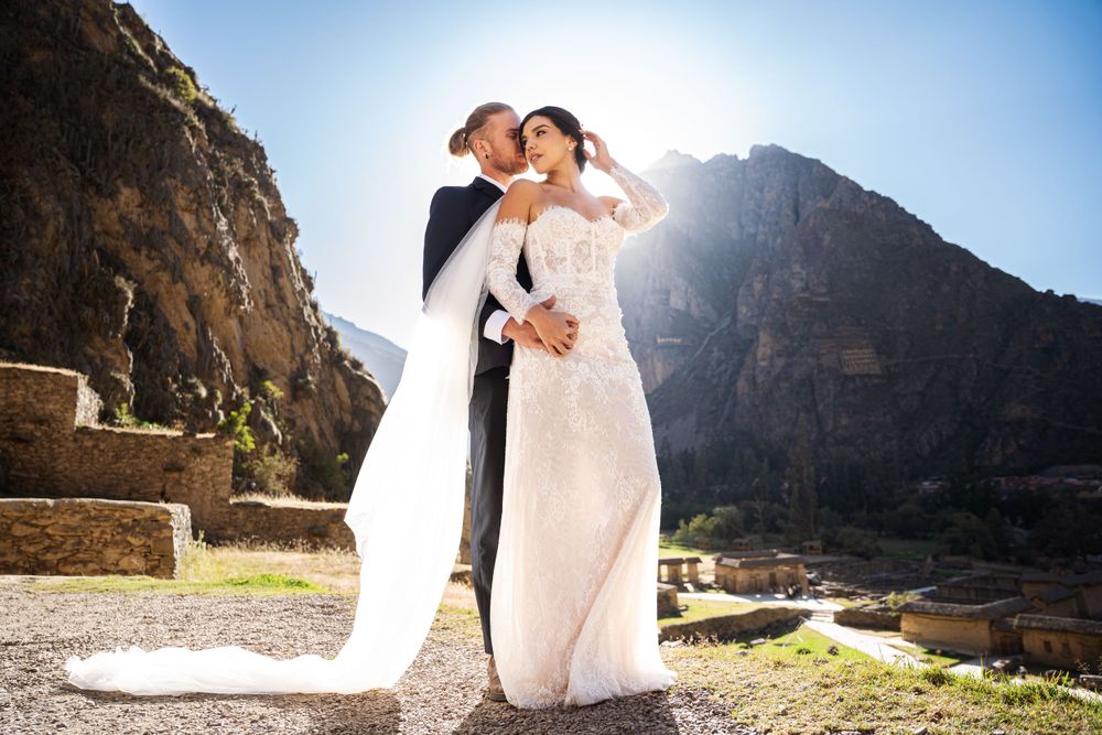 A wedding couple embracing in front of dramatic mountain cliffs with sunlight behind them.