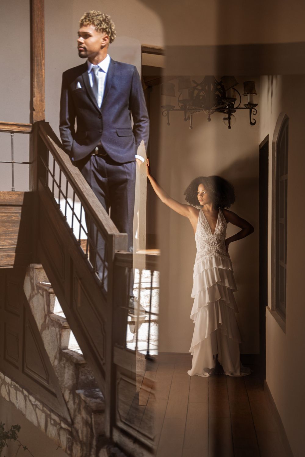 Elegant wedding photo with groom on stairs and bride posing in hallway.