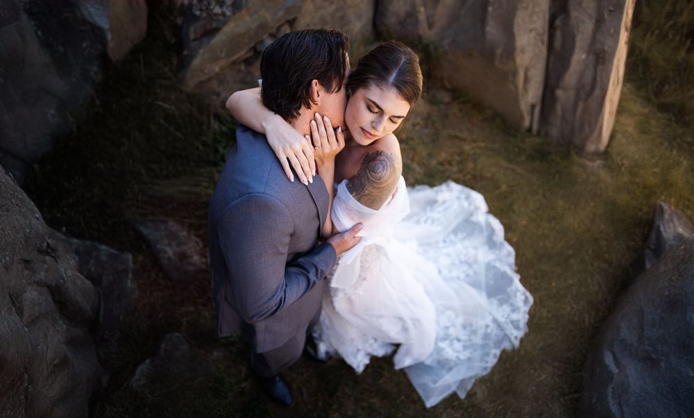Intimate wedding couple moment captured against rocky backdrop in dramatic lighting.