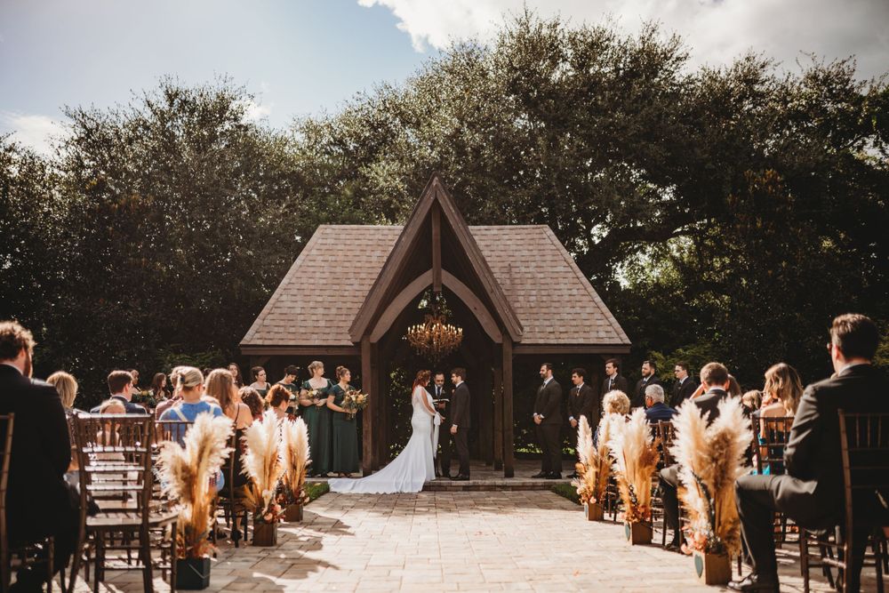 A wedding ceremony takes place under a rustic wooden chapel surrounded by trees.
